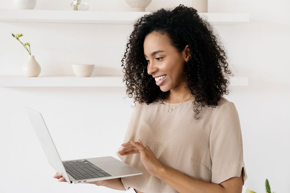 A smiling woman working on a laptop in a bright room